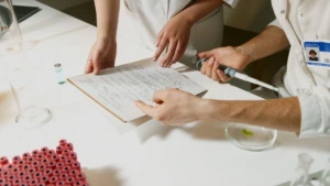 Mokslininkai baltais chalatais žiūri dokumentus laboratorijos aplinkoje